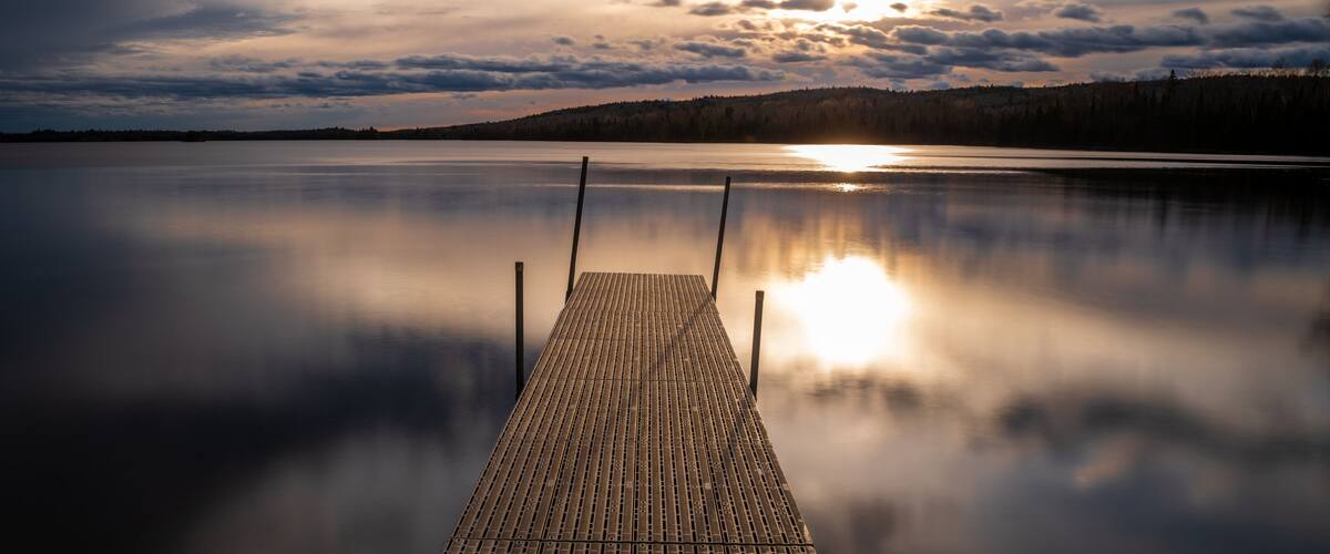 A wooden dock extending into a calm lake with a sunset in the background.