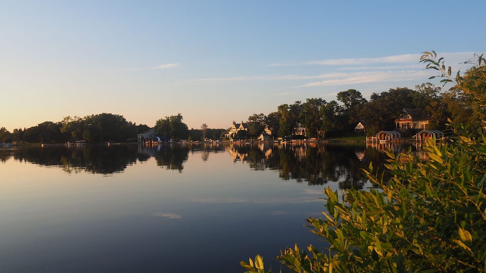 A calm lake with reflections of buildings and trees at sunset.