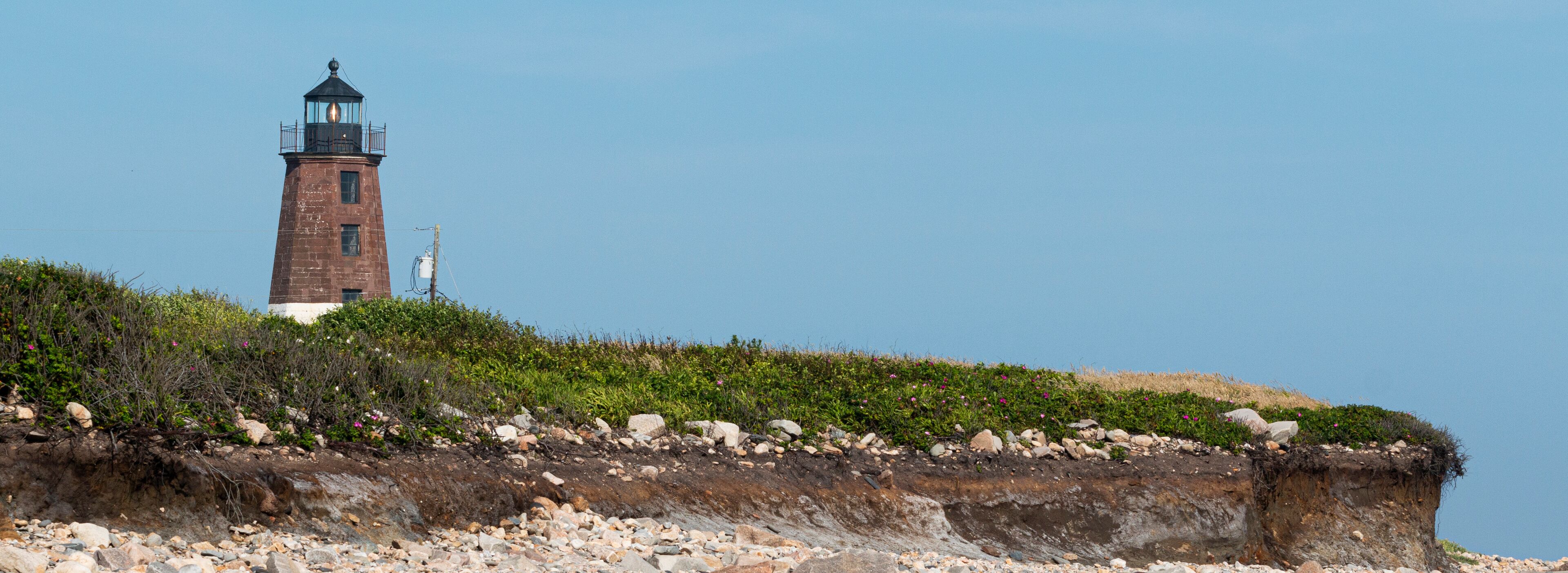 A lighthouse on a rocky cliff with sparse vegetation.