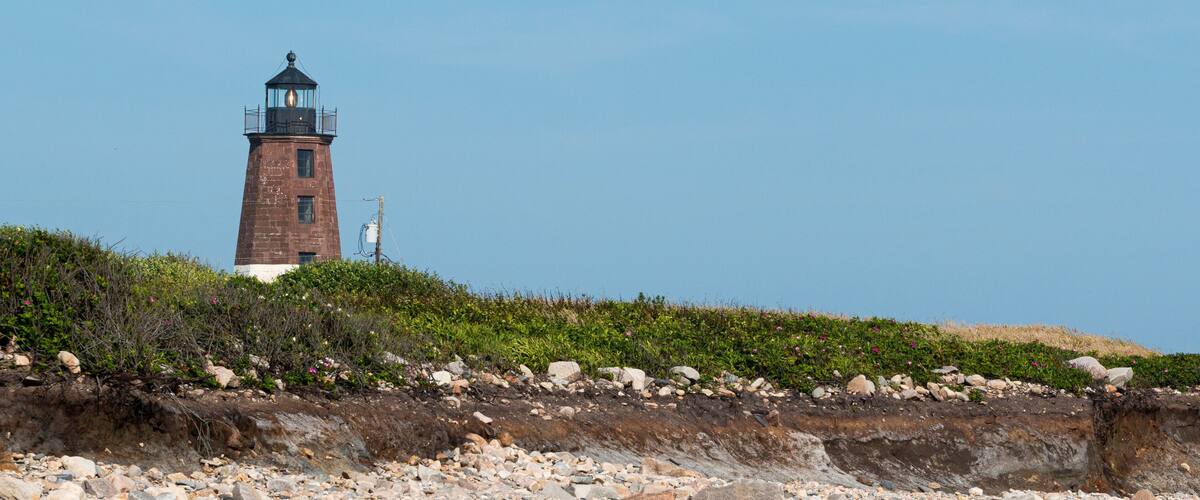 A lighthouse on a rocky cliff with sparse vegetation.