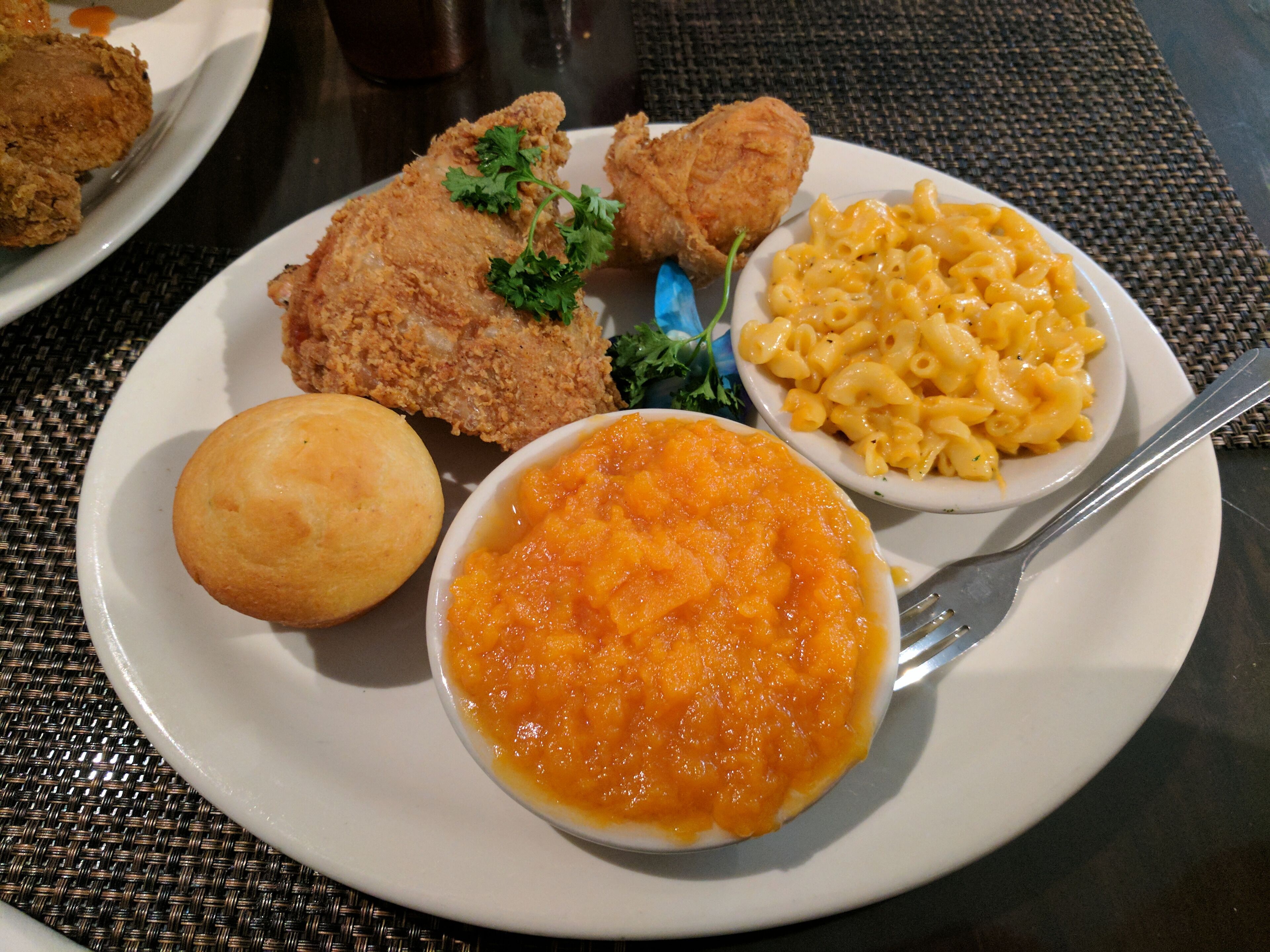 A plate with fried chicken, macaroni and cheese, a biscuit, and a bowl of soup.