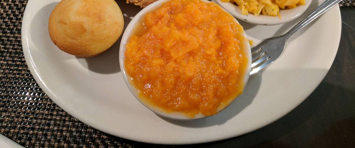 A plate with fried chicken, macaroni and cheese, a biscuit, and a bowl of soup.
