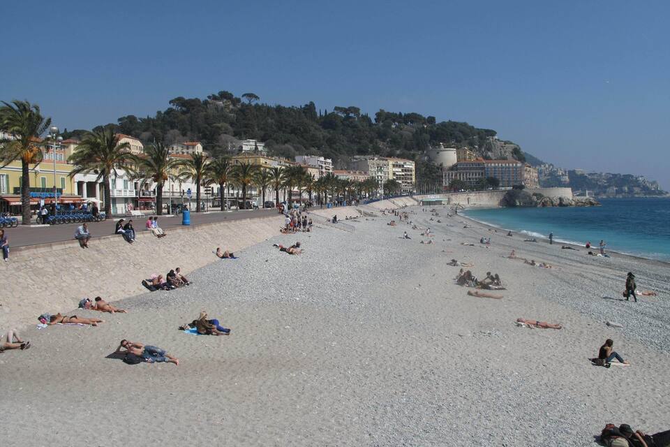 Ampia spiaggia ciottolosa con persone che prendono il sole e nuotano.
