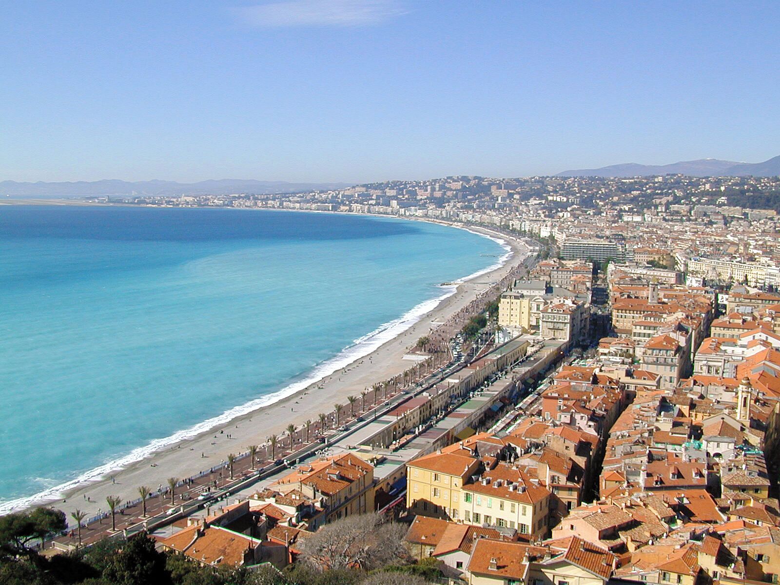 Una ciudad costera con playa, edificios y montañas a lo lejos.