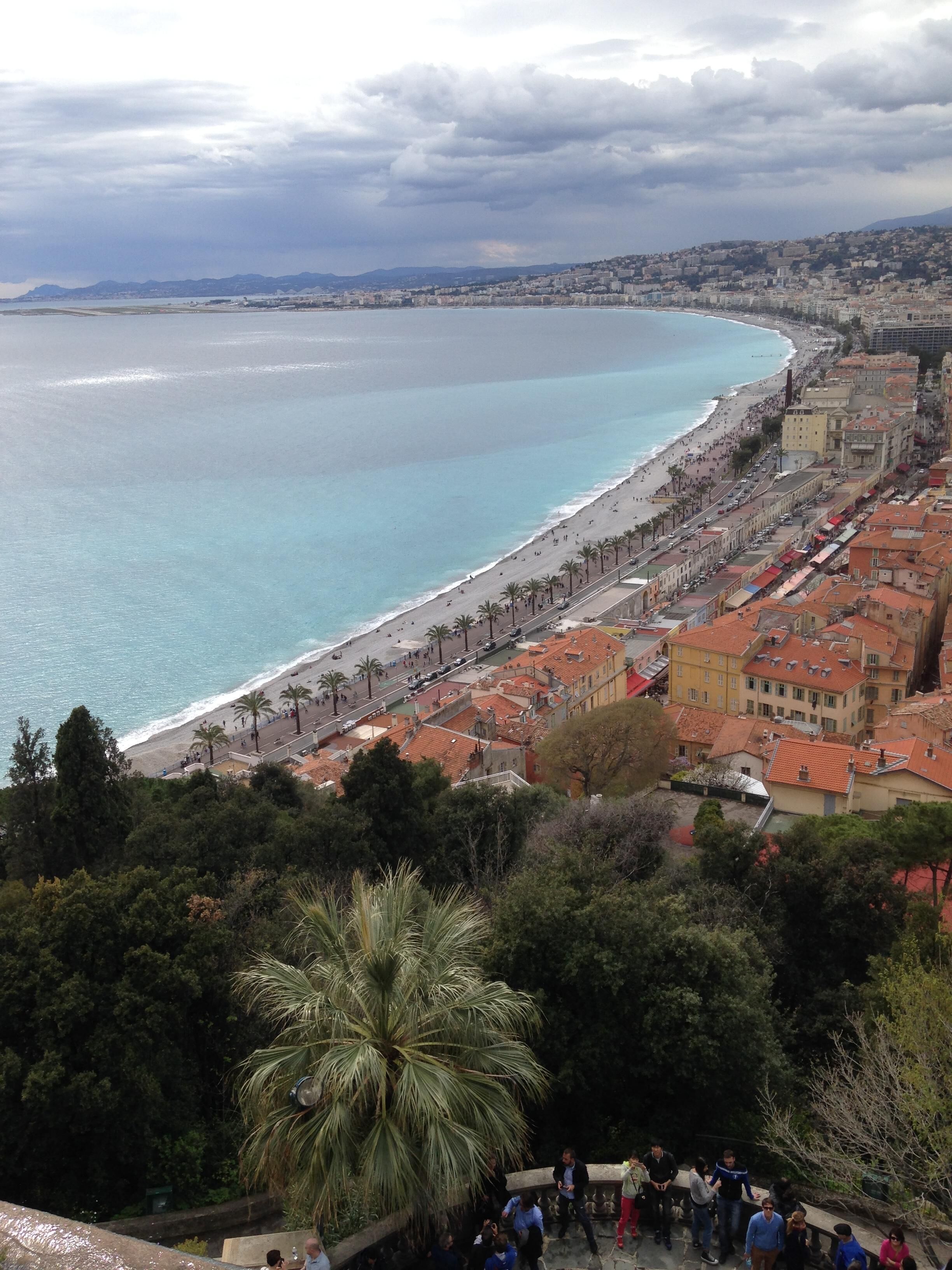 A coastal city with a beach, palm trees, and red-roofed buildings.