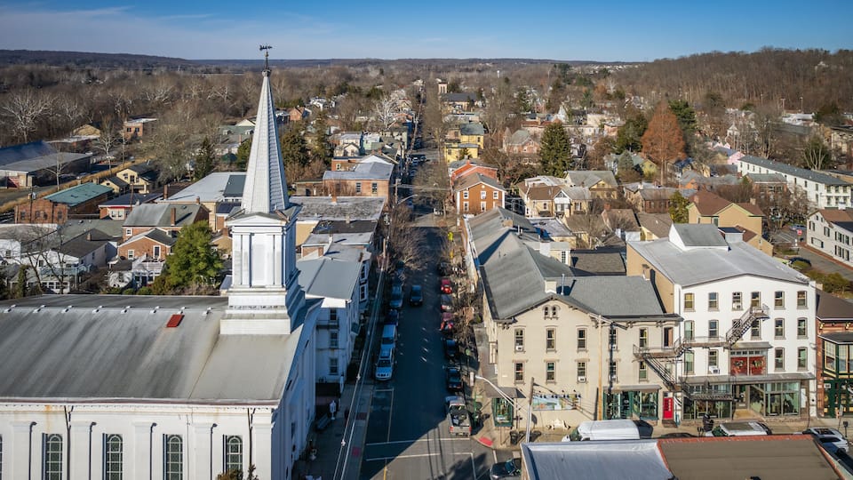 A town with a prominent church steeple, a main street lined with parked cars, and various buildings.