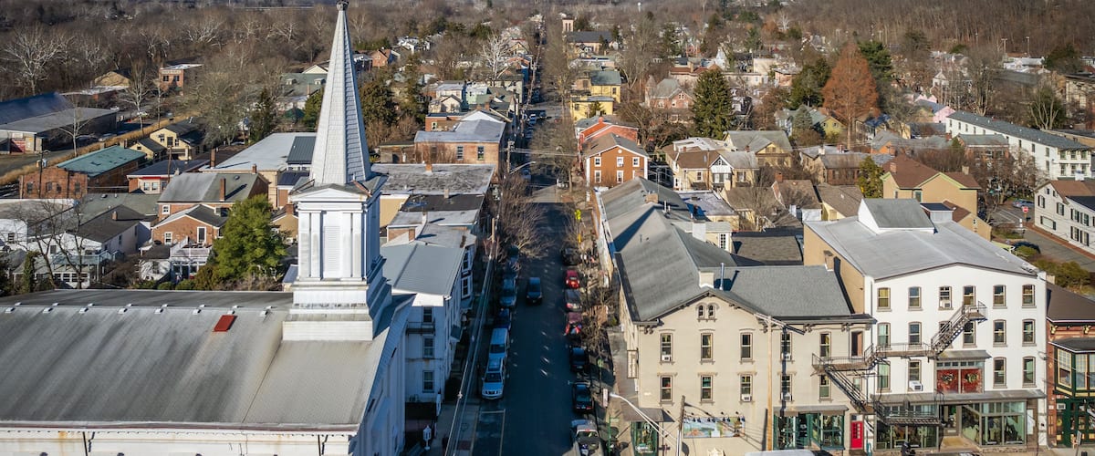 A town with a prominent church steeple, a main street lined with parked cars, and various buildings.