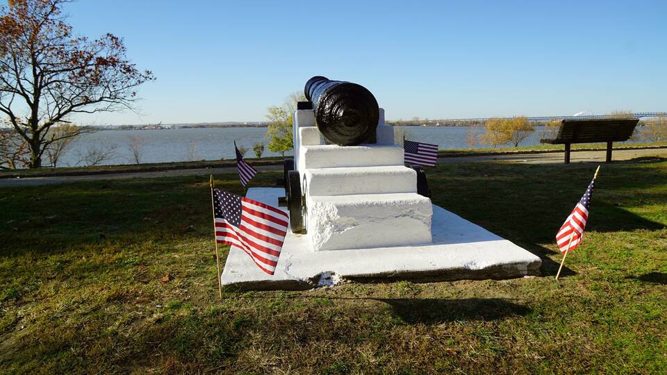 A monument with a cannon, surrounded by grass and two American flags.
