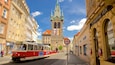 A tram on a street with historic buildings and a church tower in the background.