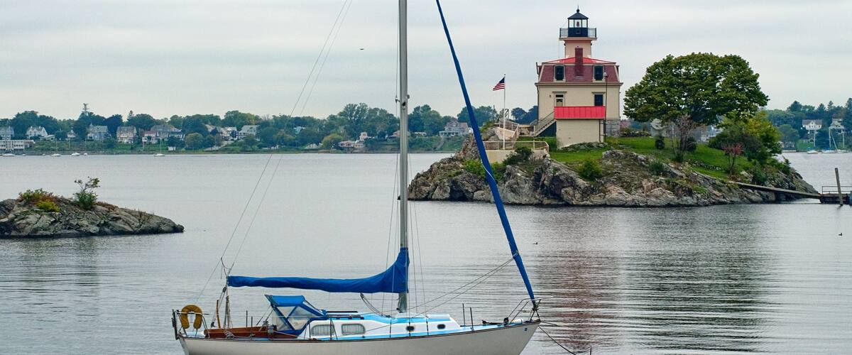 A sailboat anchored near a lighthouse on a calm body of water.