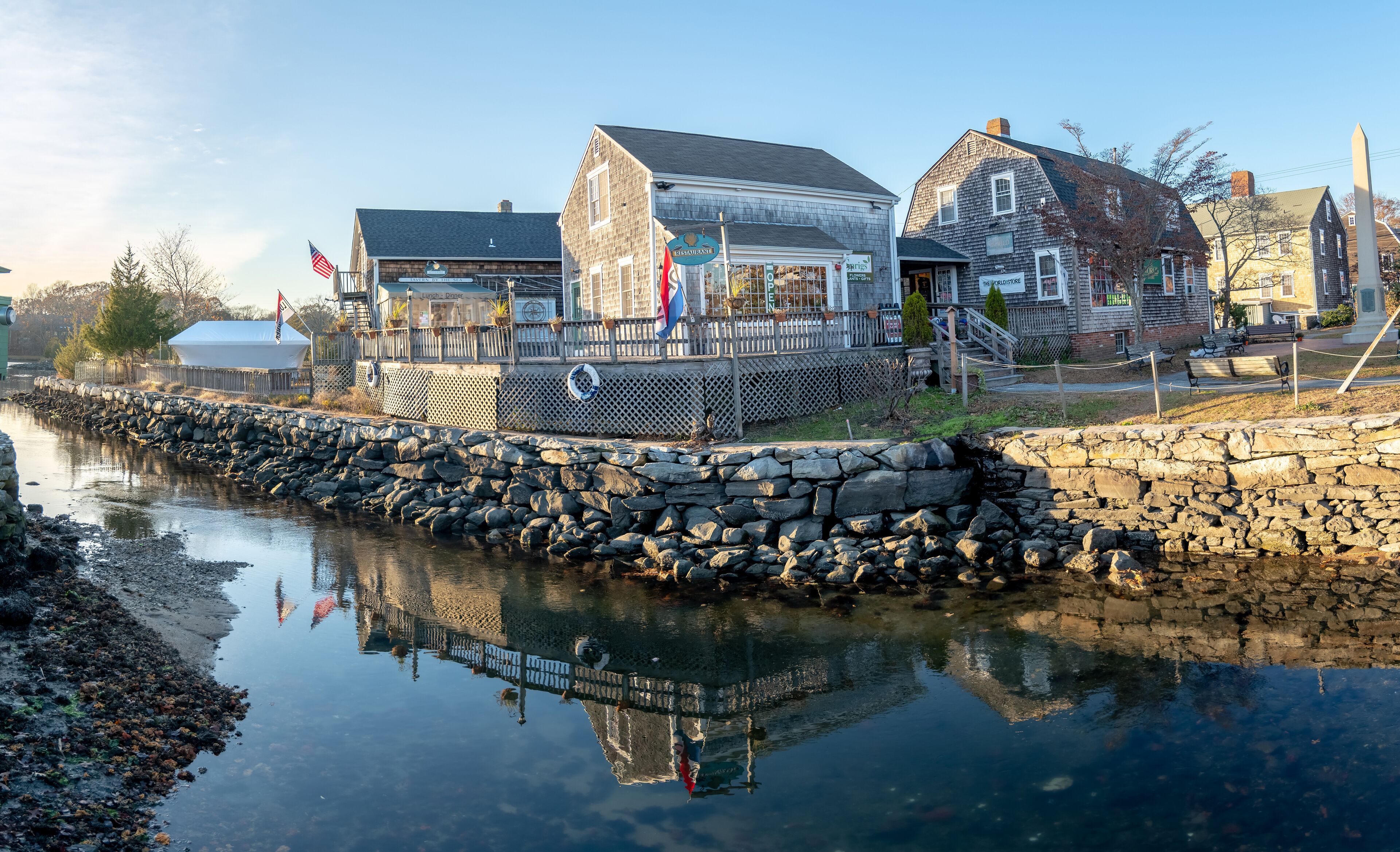 A waterfront town with stone walls, a wooden pier, and buildings with signs like 'Restaurant' and 'Lighthouse'.