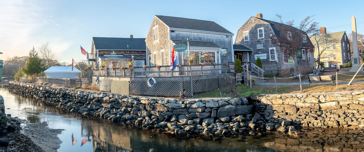A waterfront town with stone walls, a wooden pier, and buildings with signs like 'Restaurant' and 'Lighthouse'.
