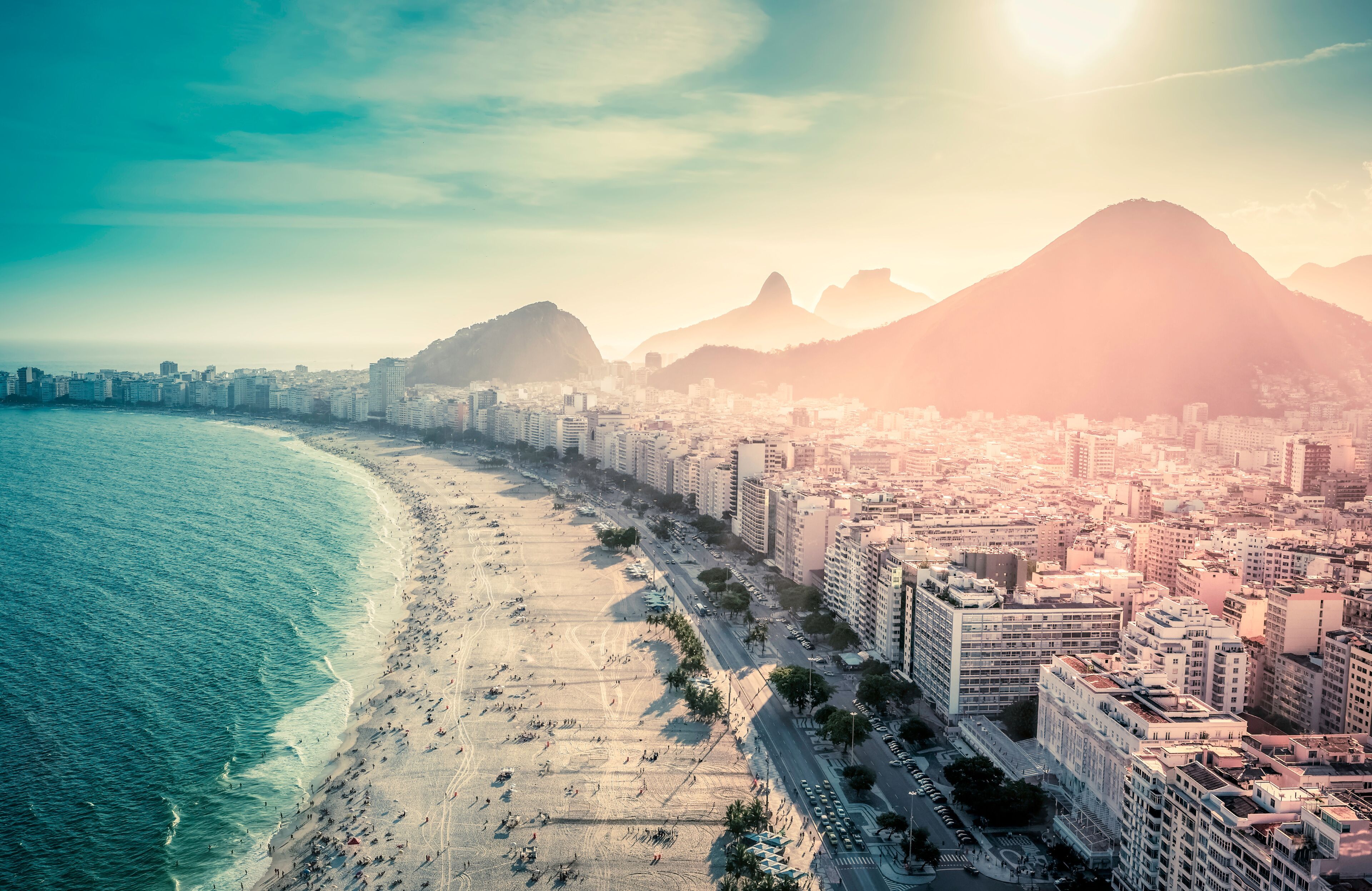 A coastal cityscape with a beach, high-rise buildings, and a prominent mountain in the background.