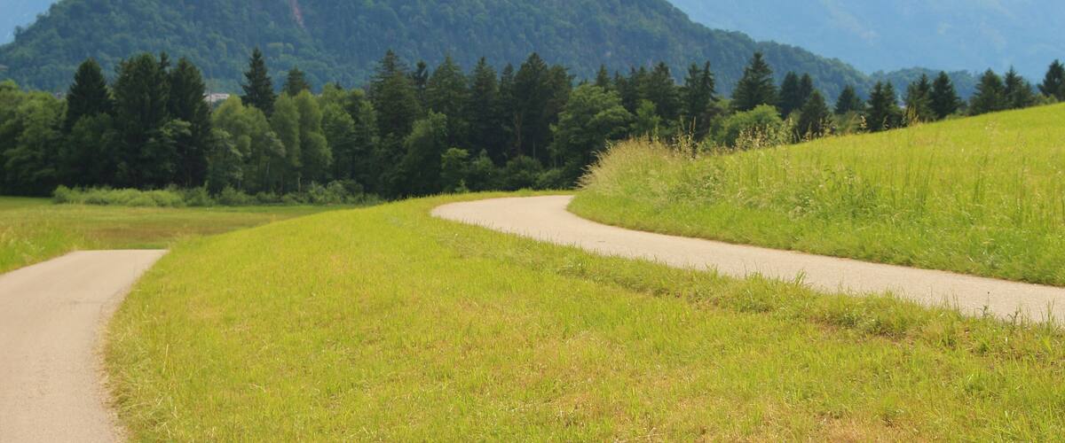 A winding road through a green landscape with mountains in the background.