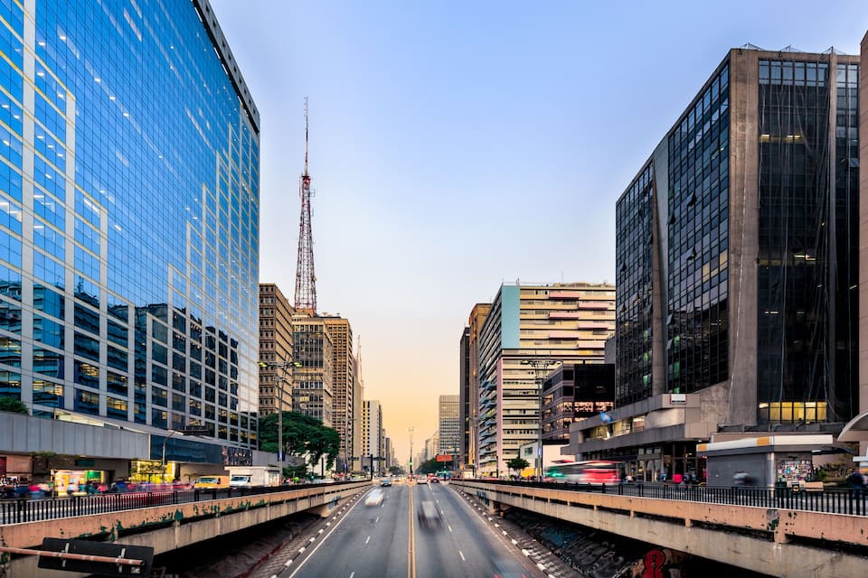 A city street with modern buildings, a bridge, and a clear sky.