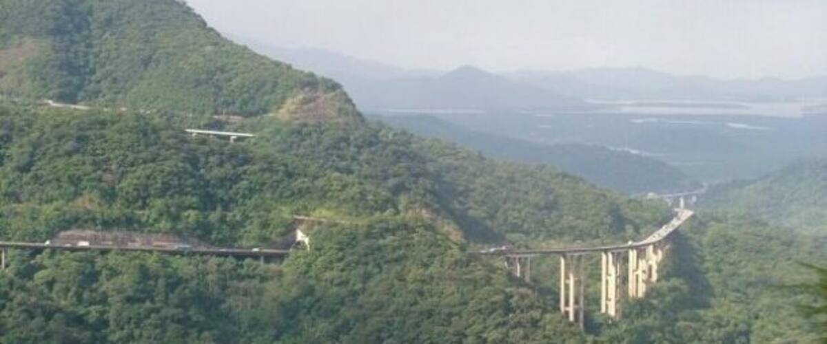 A bridge spanning a valley with lush green hills.