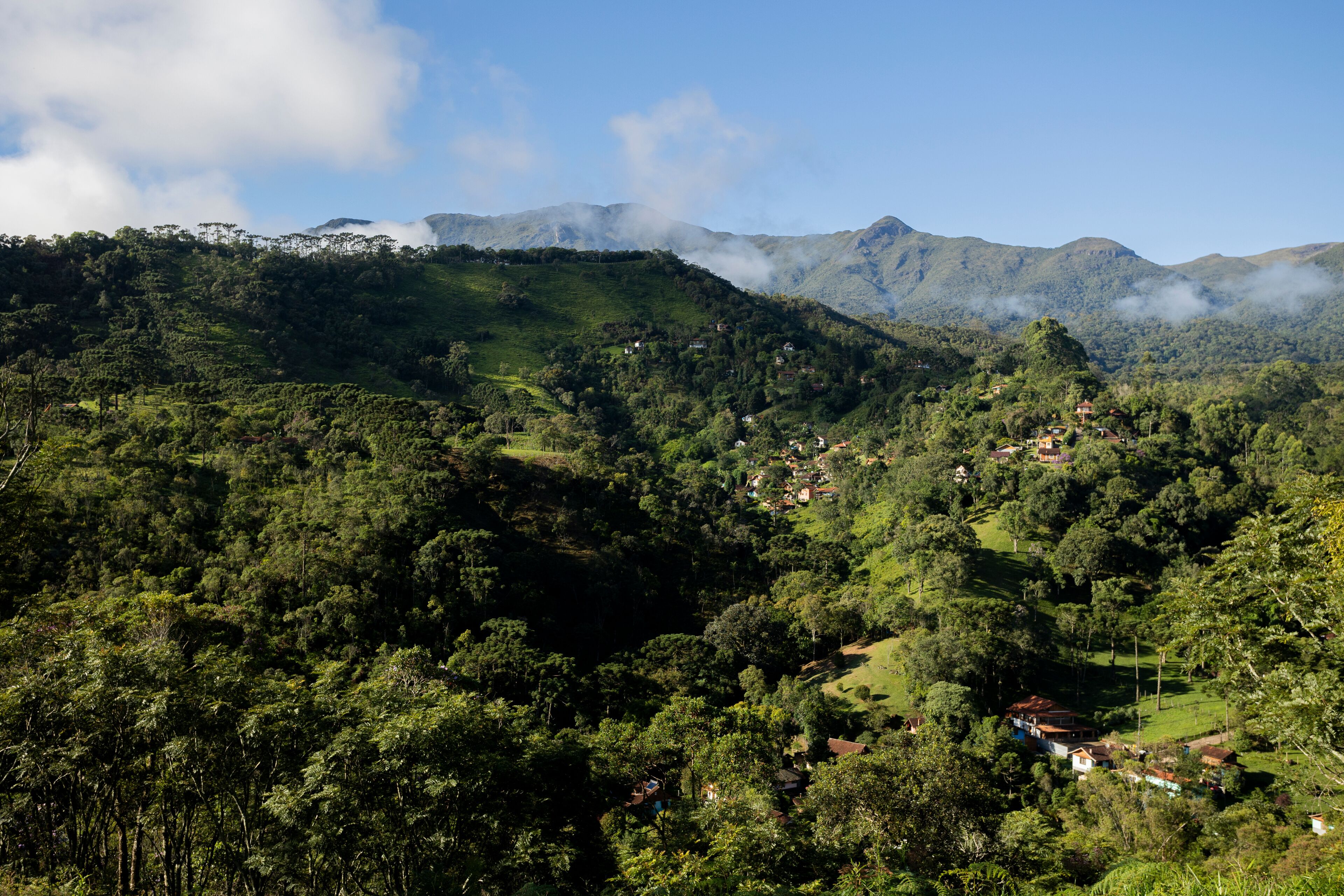 A lush valley with dense greenery, scattered houses, and mist-covered mountains in the background.
