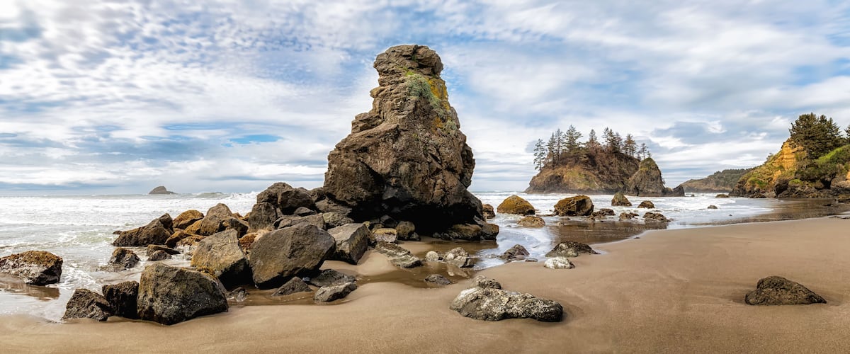 A rocky coastline with a prominent rock formation, sandy beach, and ocean waves.