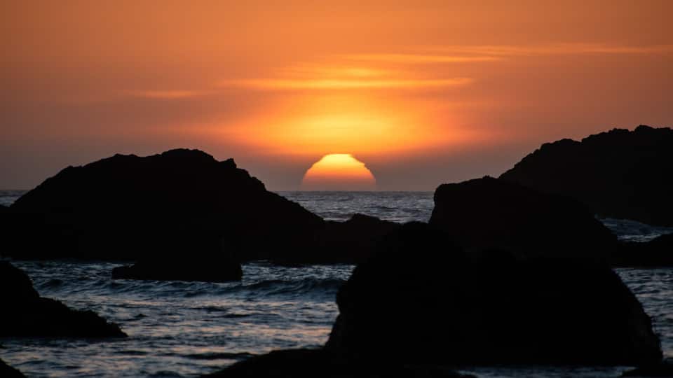 A sunset over the ocean with rocky formations in the foreground.