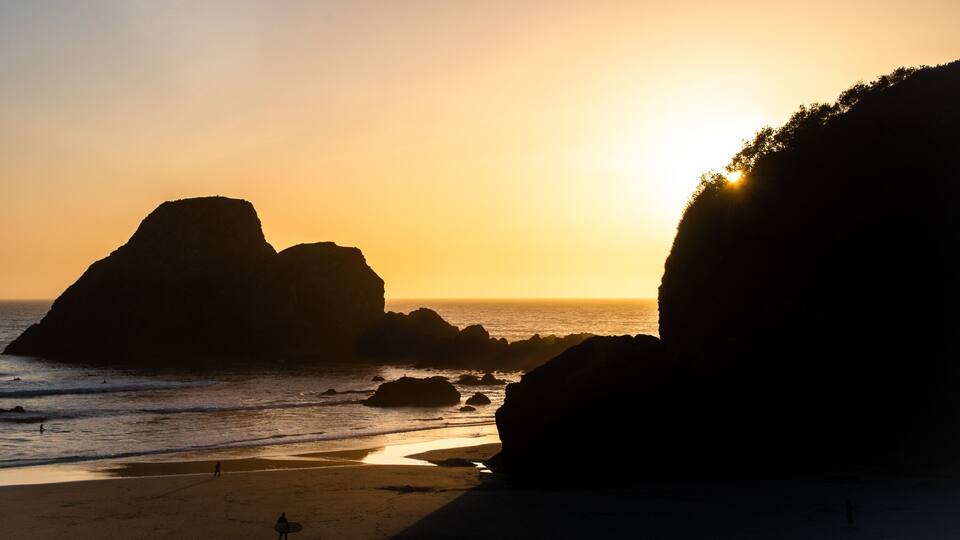 A beach with large rock formations and the ocean at sunset.
