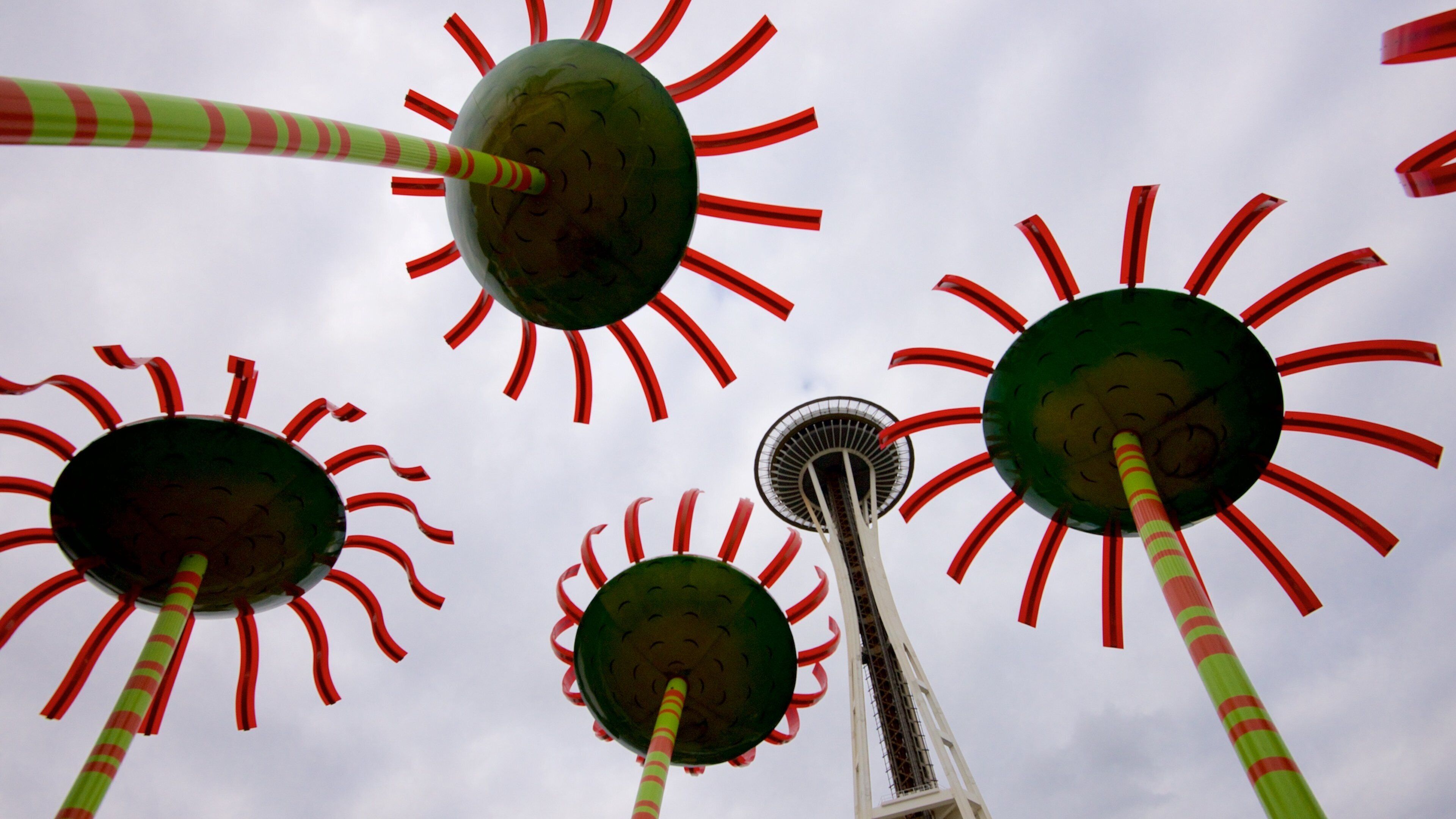 A Ferris wheel with red and green striped poles and spherical gondolas against a cloudy sky.