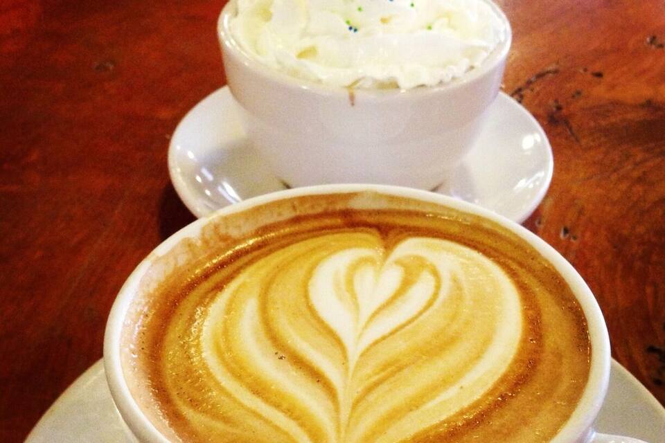 Uma chávena de café com arte de latte e uma taça de chantilly com confeitos.