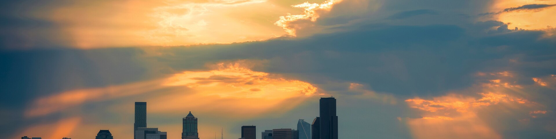 Horizonte urbano ao pôr do sol, com um rio em primeiro plano e um barco.
