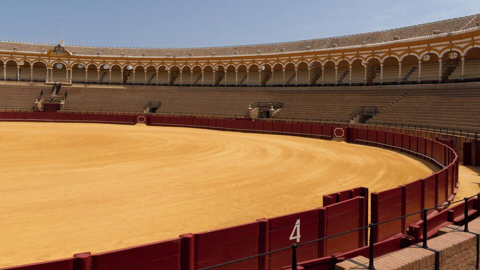 Una plaça de toros amb terra de sorra i seients vermells.