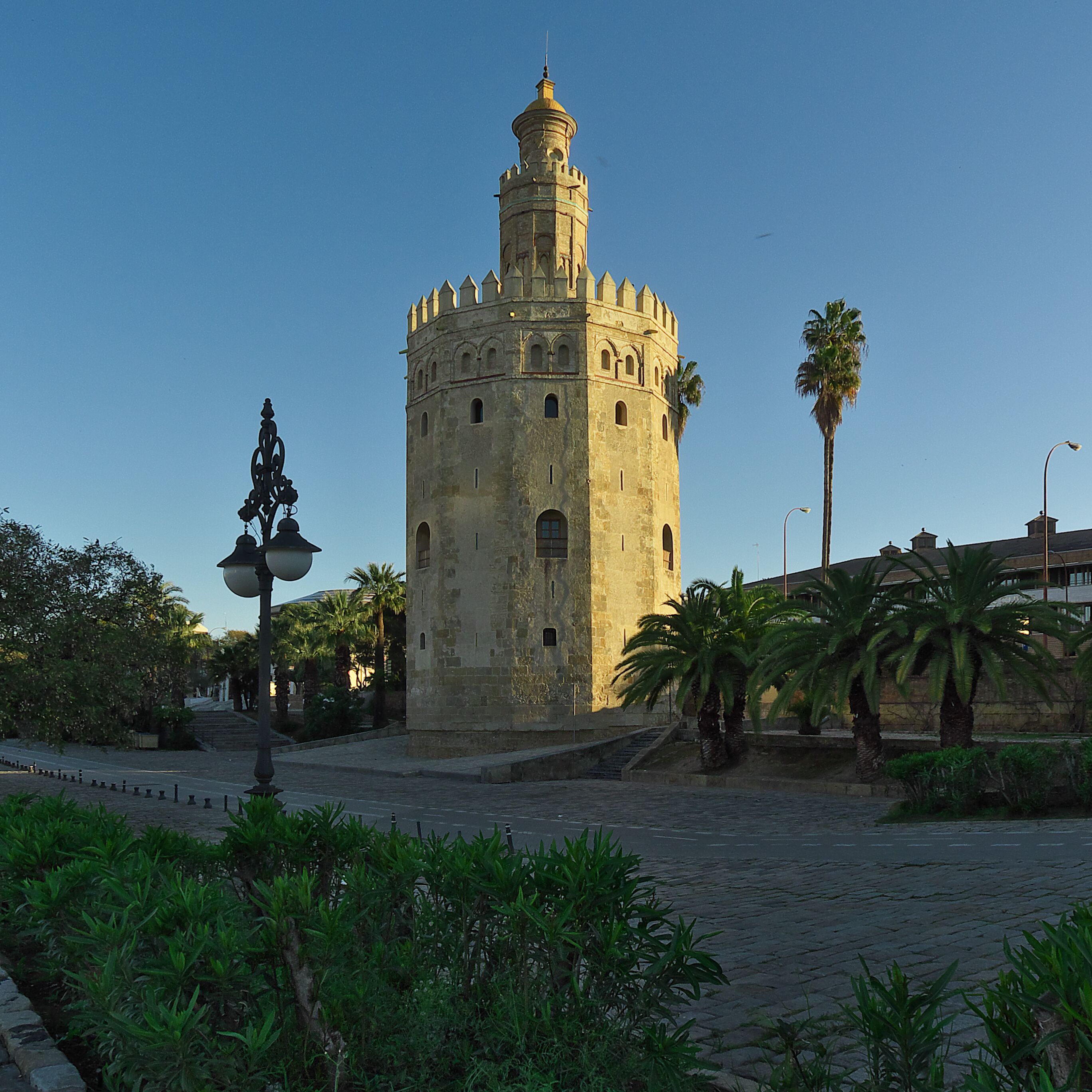 A historic tower with a dome and battlements, surrounded by palm trees and cobblestone pavement.
