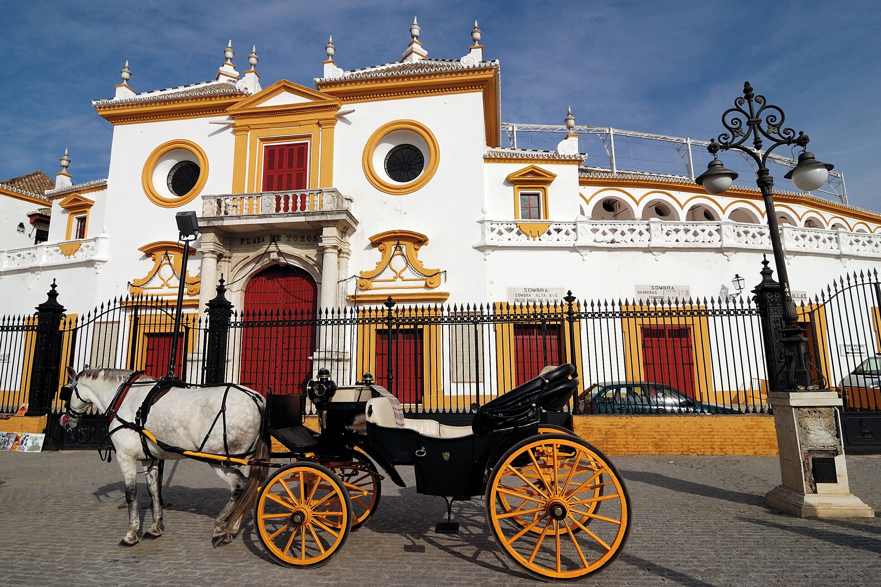 A white building with yellow trim and red doors, a horse-drawn carriage, and a fence.