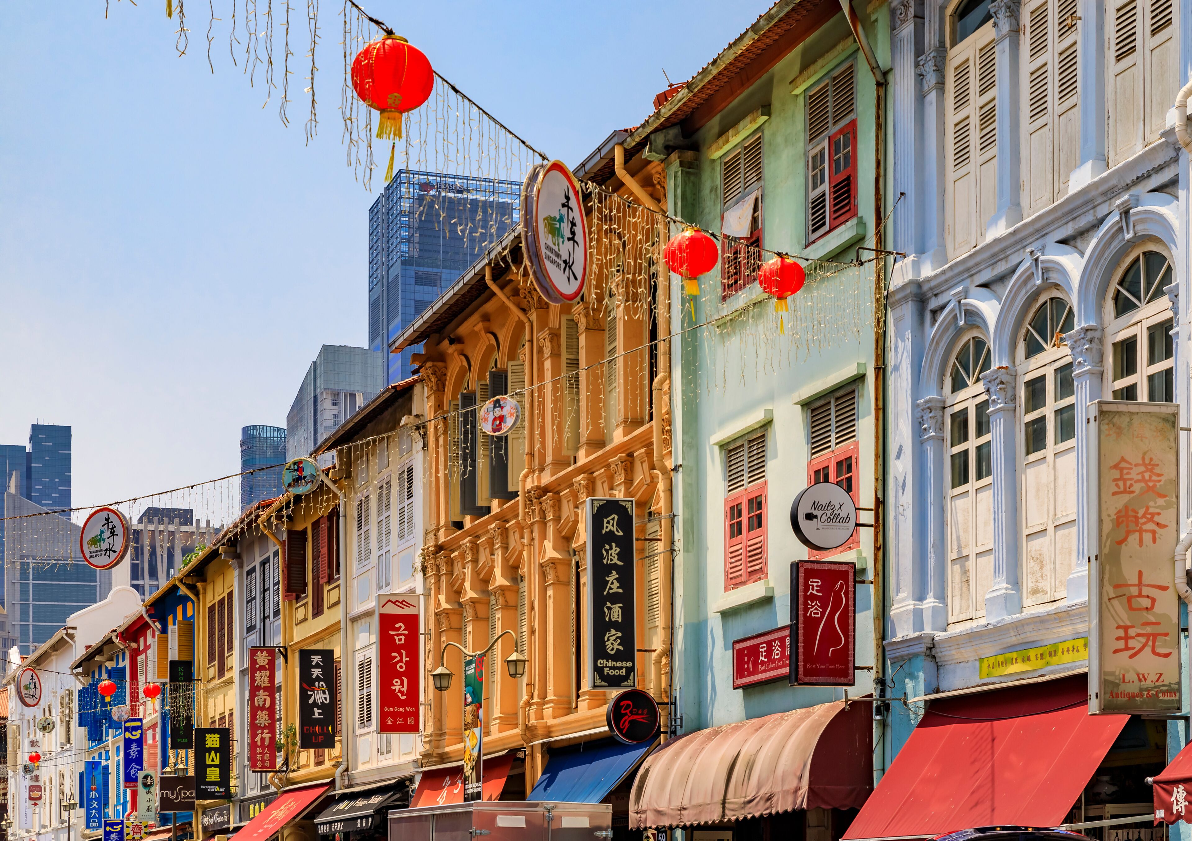 A row of colorful buildings with traditional Chinese signage, a clear blue sky, and modern skyscrapers in the background.
