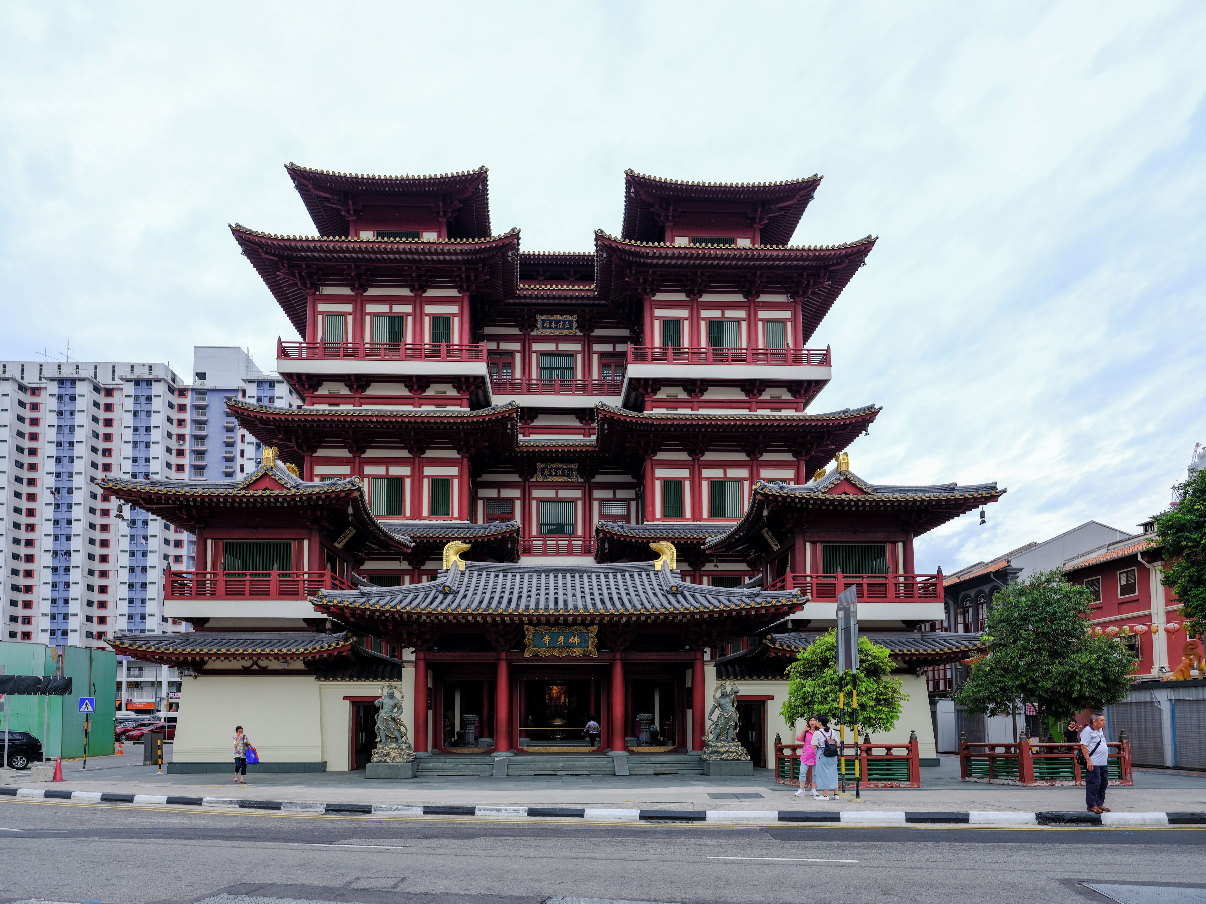 Una pagoda tradicional de varios niveles con detalles en rojo y oro, frente a un fondo de edificios modernos.