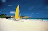 A beach with a sailboat, people, and a clear blue sky.