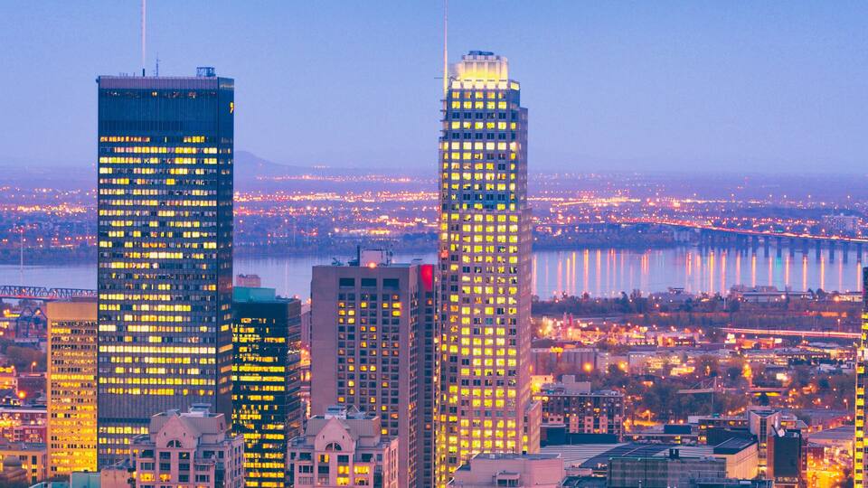 A cityscape with illuminated skyscrapers, a river, and a bridge.
