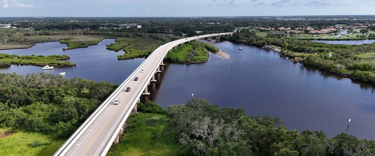 A bridge over a river with surrounding greenery and distant buildings.