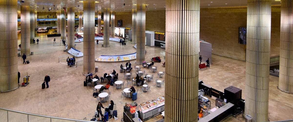A spacious airport terminal with high ceilings, large cylindrical columns, and a central information desk.