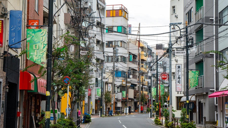 A narrow urban street lined with multi-story buildings, various signs, and electrical wires.