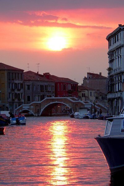 Atardecer sobre un canal con un puente, barcos y edificios históricos.