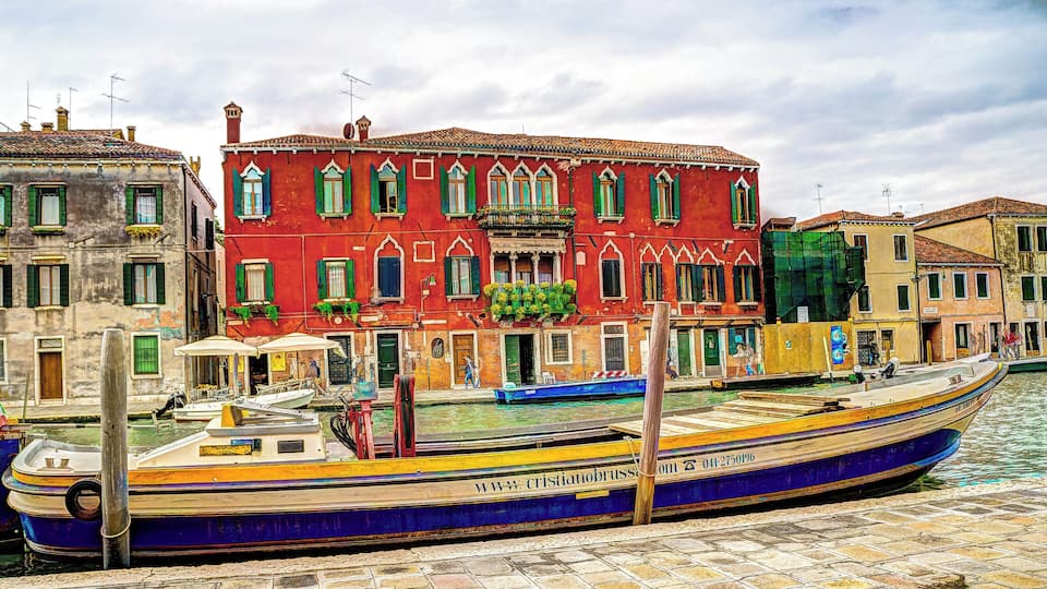 Uma embarcação veneziana colorida atracada num canal, com edifícios tradicionais ao fundo.