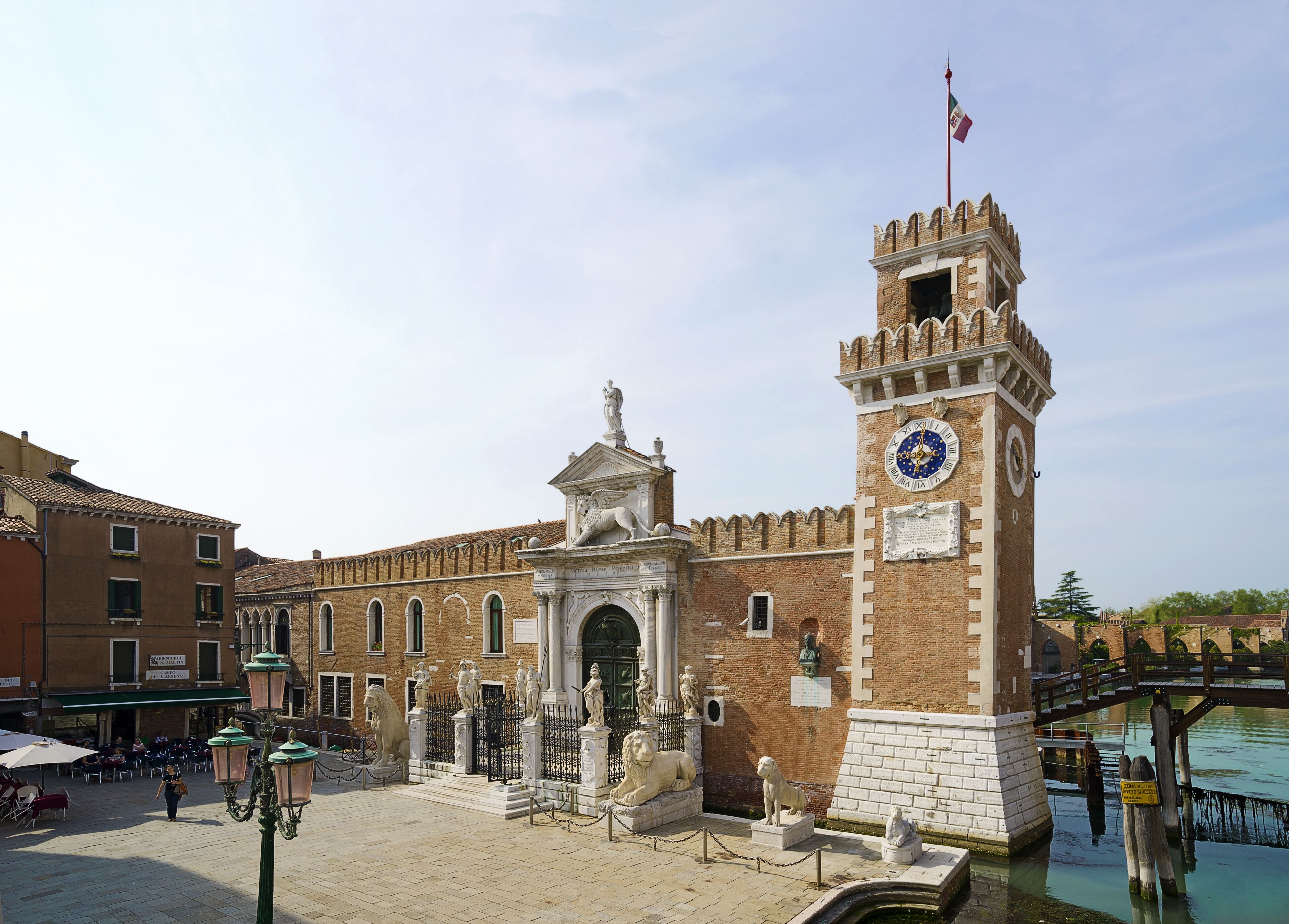 Un edificio histórico con una torre de reloj, estatuas y un puente sobre el agua.