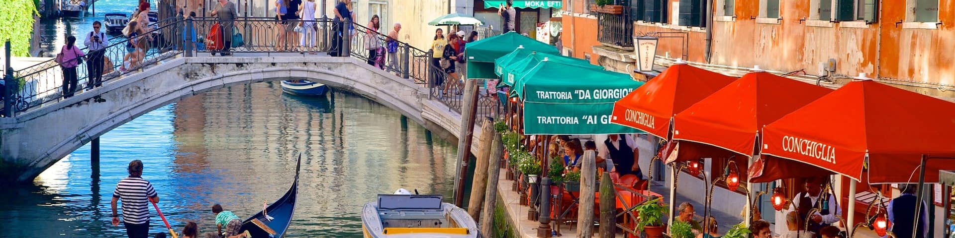 A canal with gondolas, a bridge, and buildings with outdoor seating.