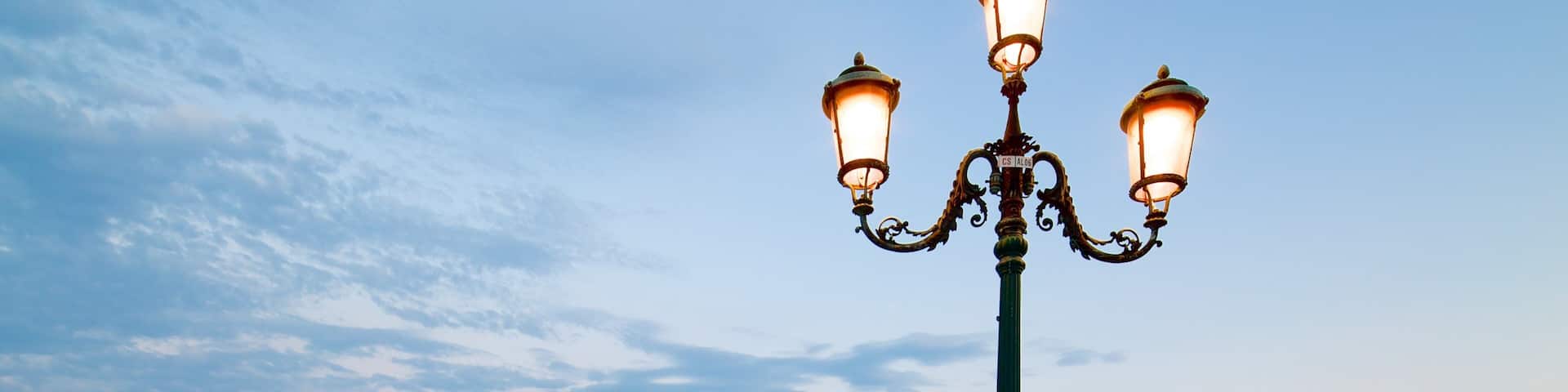 A waterfront with boats docked, a lamp post, and a historic building in the background.