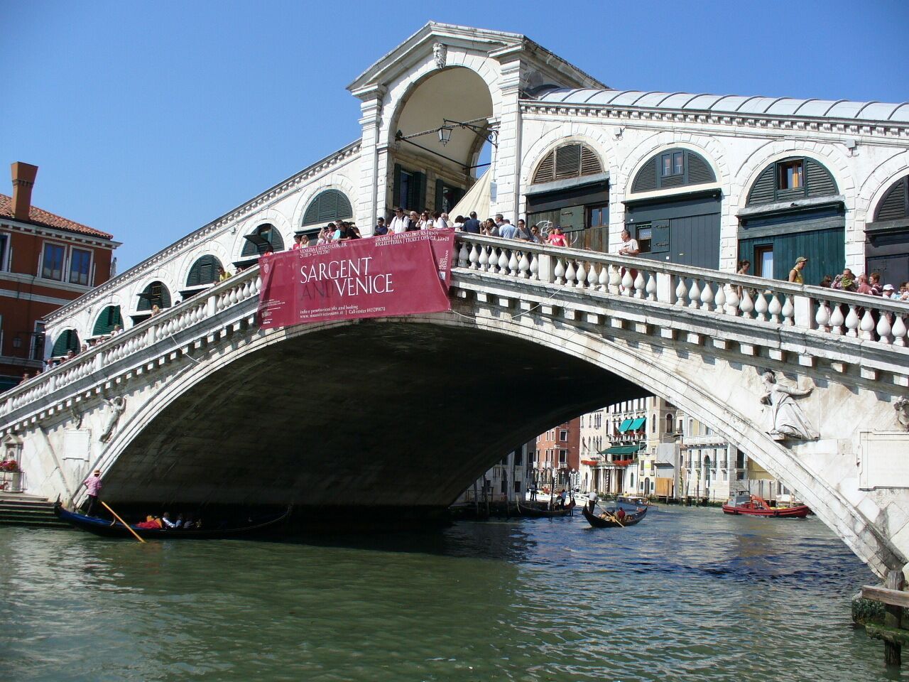 A stone bridge with a banner reading "SARGENT VENICE" over a canal with gondolas.