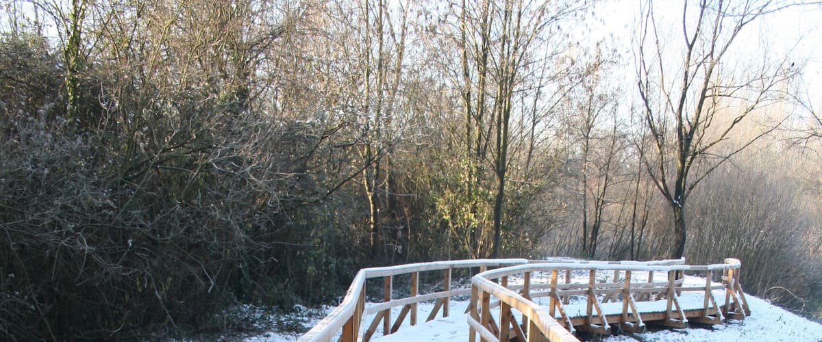 A wooden bridge over a river with snow on the planks and railings.