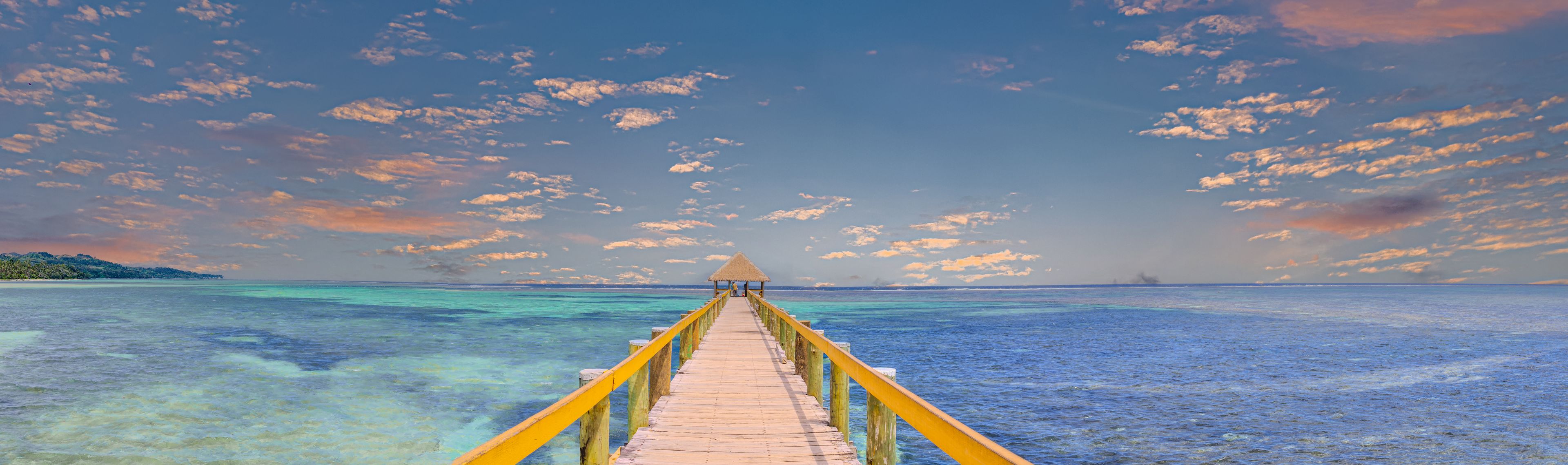 A wooden pier leading to a thatched-roof structure over turquoise waters.