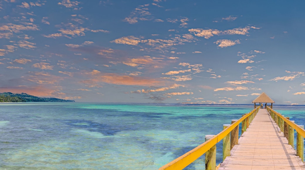 A wooden pier leading to a thatched-roof structure over turquoise waters.