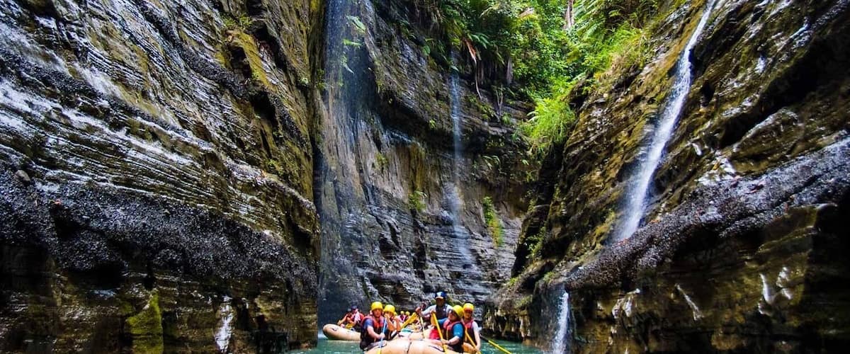 A group of people rafting through a narrow canyon with waterfalls.