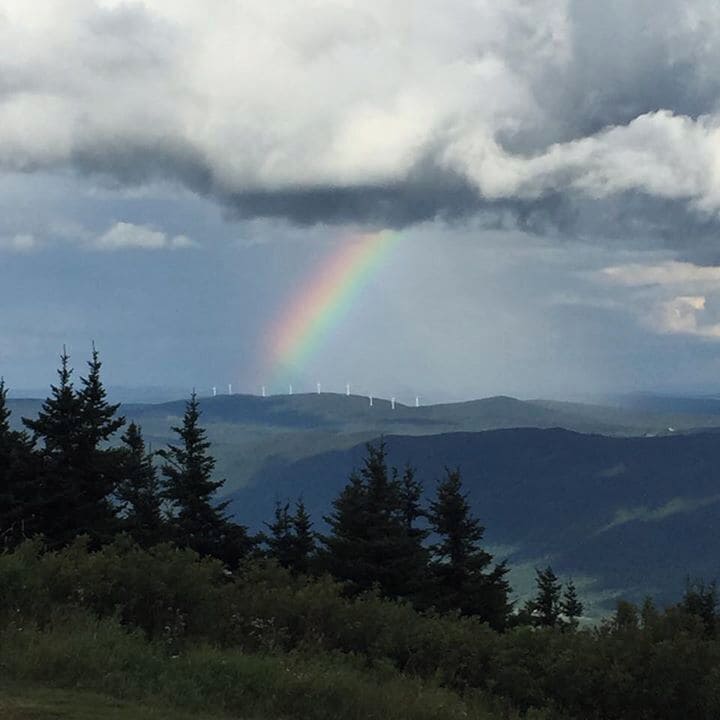 A mountain landscape with a rainbow and wind turbines in the distance.