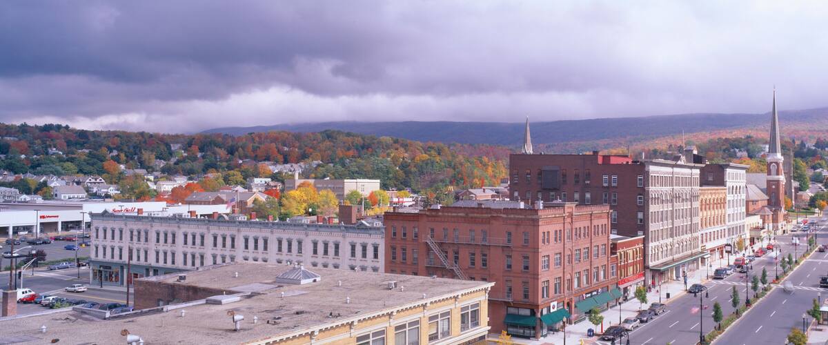 A cityscape with autumn-colored trees, historic buildings, and a mountainous backdrop.