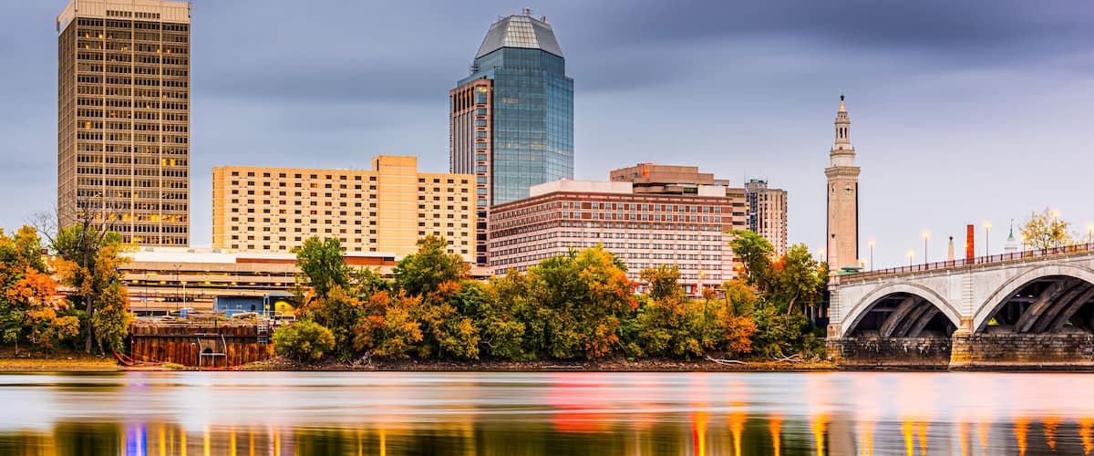 A city skyline with a mix of modern and historic buildings, a bridge, and a river reflecting the structures.